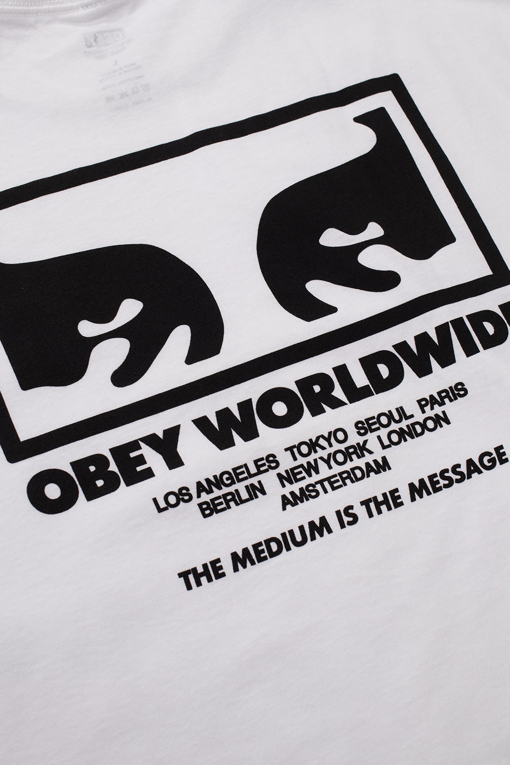 Macro detail view of the solid black Obey bold font logo printed across the fine white 100% cotton jersey fabric on the front chest.