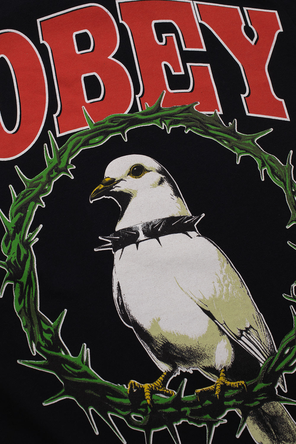 Detailed close-up shot of the front screen print on the black Obey Thorns Of Peace tee, showcasing the white peace dove with a black studded choker necklace perched inside a sharp green thorn wreath below bold red Obey typography.