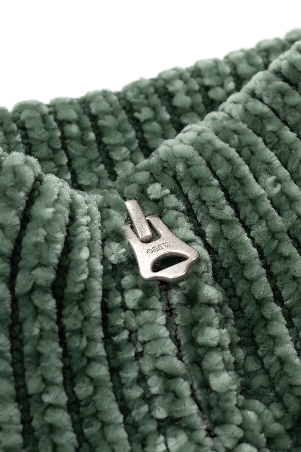 Macro detail shot of the antiqued silver metal zipper pull engraved with the Obey brand text logo, nestled inside the thick green chenille ribbed knit collar of the Obey Varen sweater.