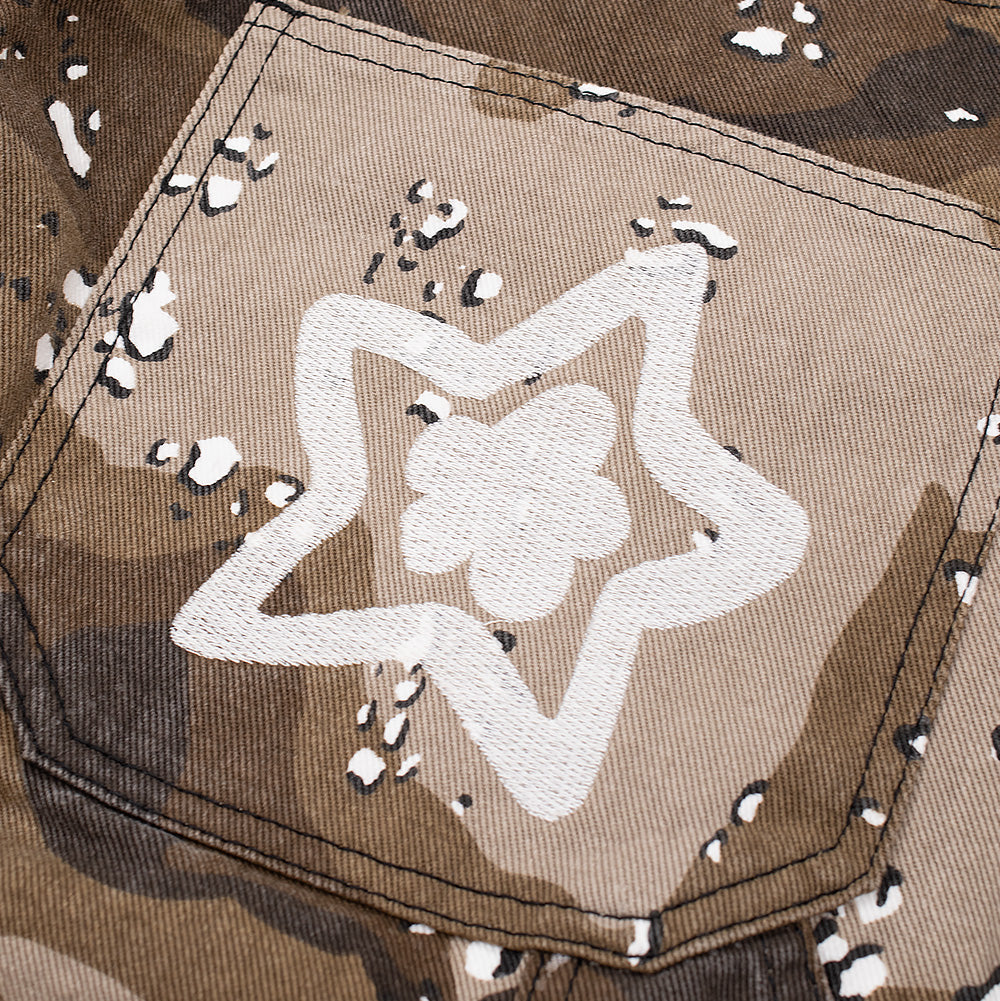 Detailed macro perspective of the back right pocket embroidery on the Starteam East Village Chocolate Chip Camo Jeans, showcasing the thick, raised white chain-stitch embroidery tracing a five-pointed outline star around an inner floral star icon against the chocolate chip camo background.