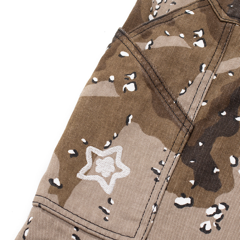 Close-up shot of the utility carpenter tool pocket on the outer leg of the Starteam Chocolate Chip Camo Star Jeans, featuring an angled top hem, reinforced seam joinery, and a miniature white embroidered Starteam flower-star motif centered on the speckled brown camouflage cotton canvas.