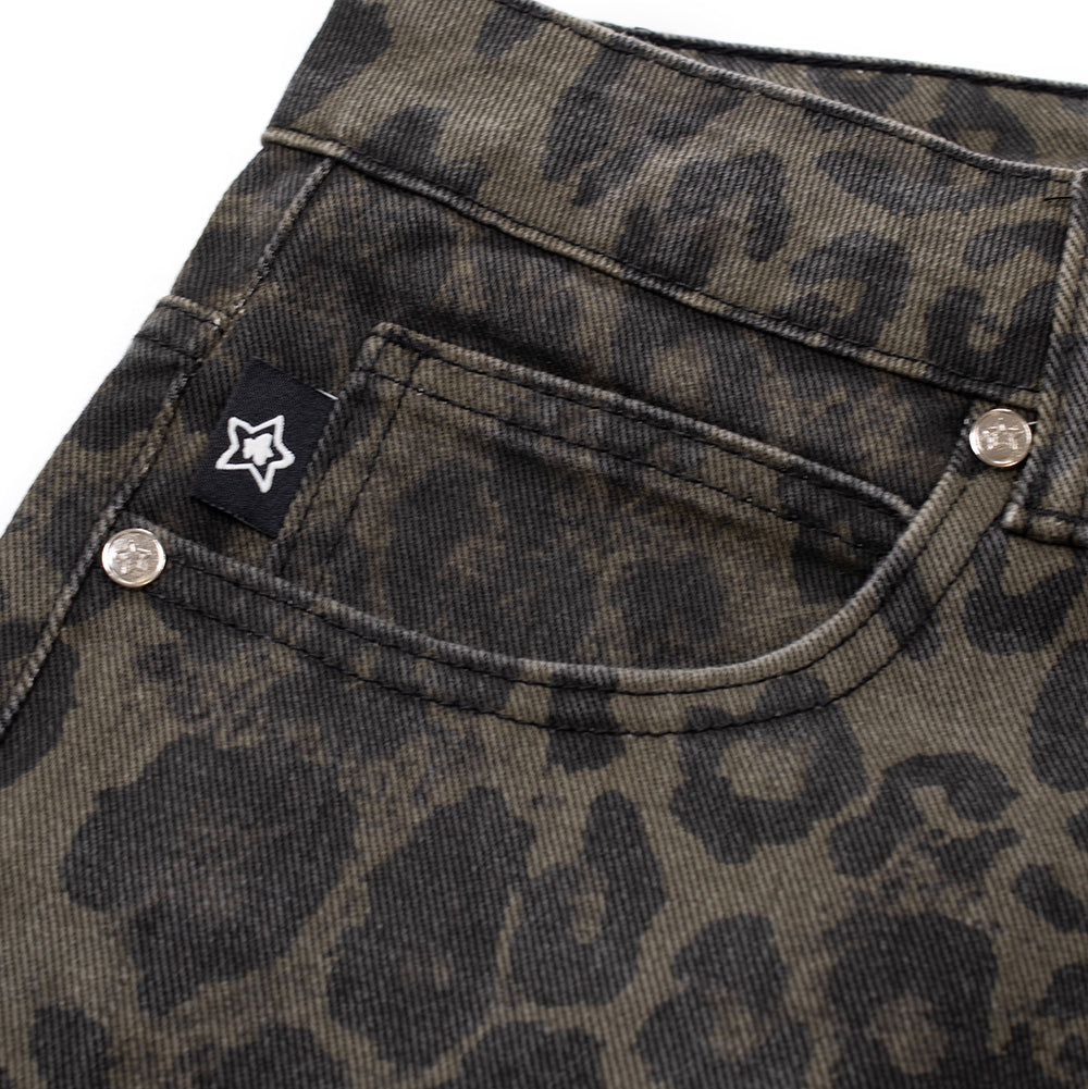 Macro studio view of the front right coin pocket on the olive Starteam East Village Jeans, displaying silver logo rivets, clean double-needle edge stitching, and a square black woven brand label decorated with a clean white embroidered star silhouette against the textured leopard pattern denim.
