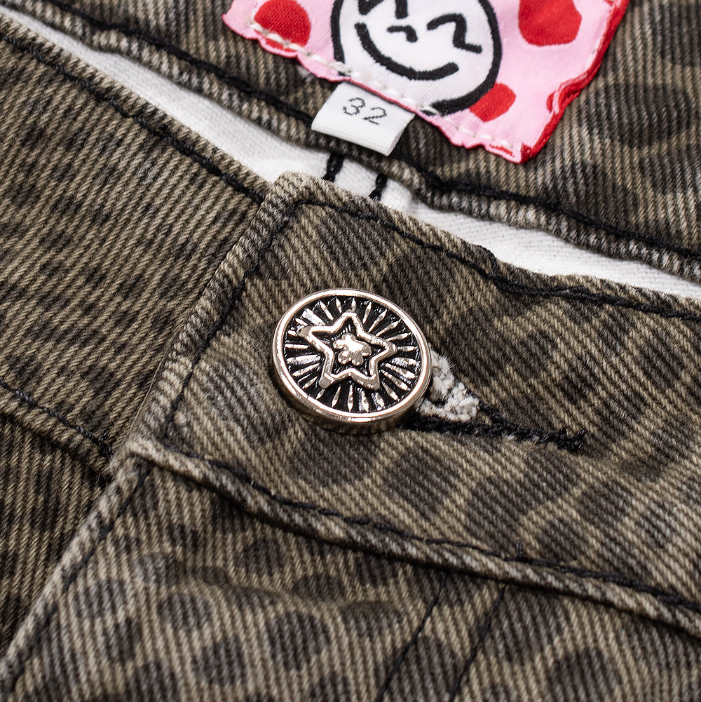 Detailed macro studio close-up of the front waistband tack button on the Starteam Snakeskin Star Jeans, showcasing the antiqued silver metal button engraved with a raised radiant Starteam star icon, set above the heavy olive diagonal twill denim fly and revealing the interior white-and-red polka-dot waistband facing with a black-and-white illustrated cartoon face label.