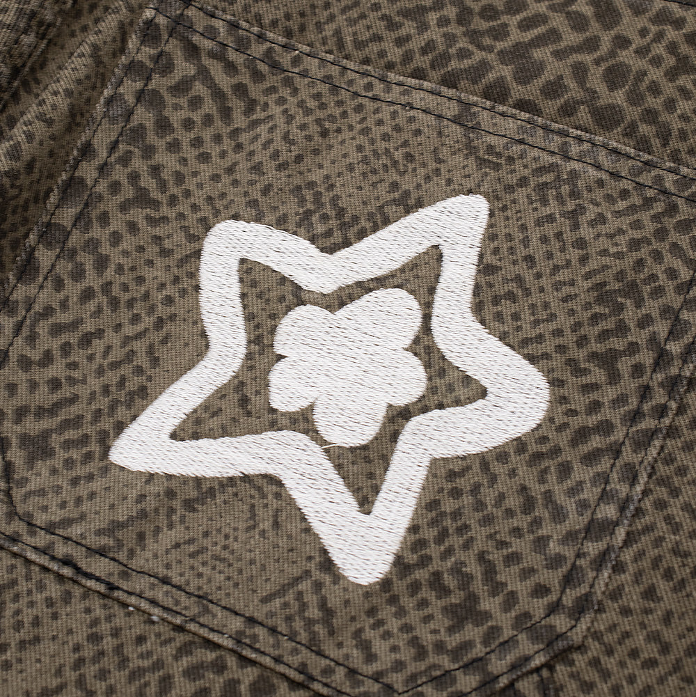 Detailed close-up shot of the rear right pocket embroidery on the Starteam East Village Snakeskin Star Jeans, focusing on the dense, raised white chain-stitch embroidery tracing a five-pointed outline star around an internal blooming floral icon over the washed olive-and-charcoal python scale pattern.