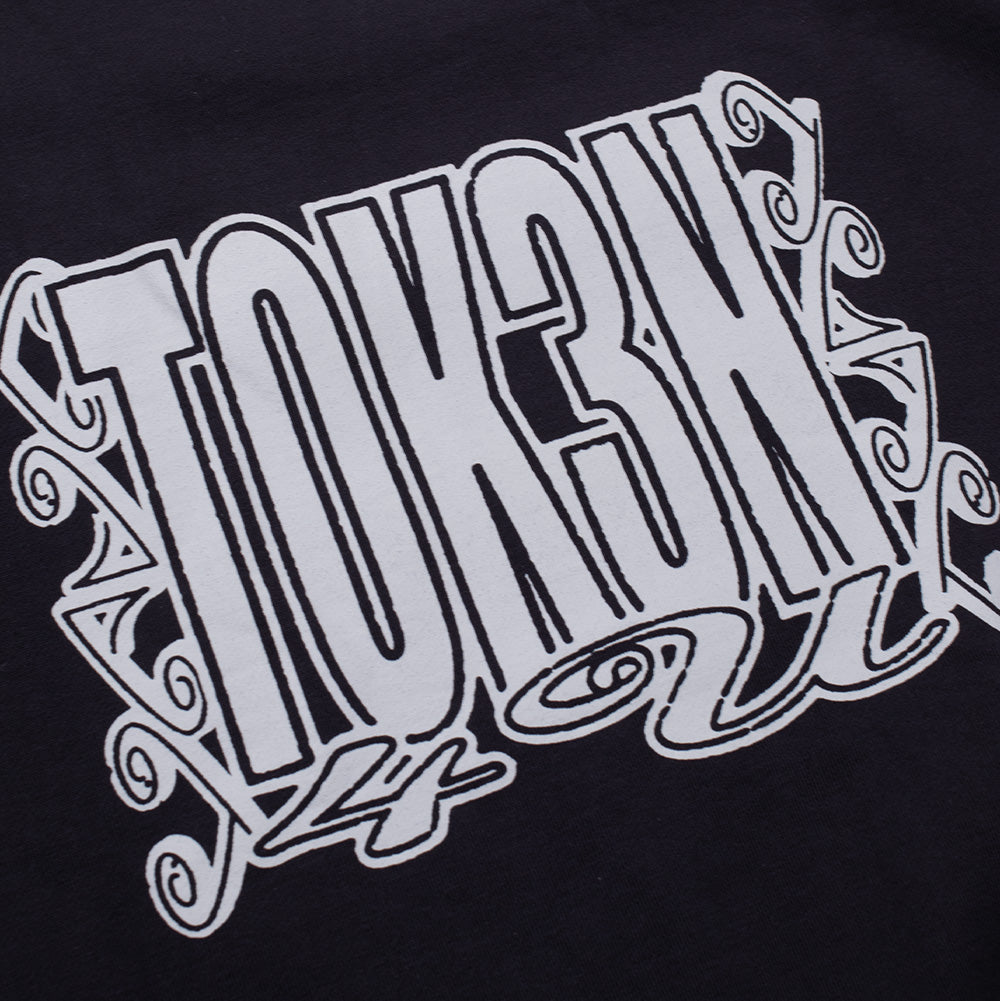 Detailed macro studio close-up of the back graphic print on the Token Grand Crewneck, highlighting the crisp white screen-printing ink texture, clean outlined bubble typography reading "TOKEN", and the decorative scrollwork frame set against the dense black loopback cotton fleece fabric.