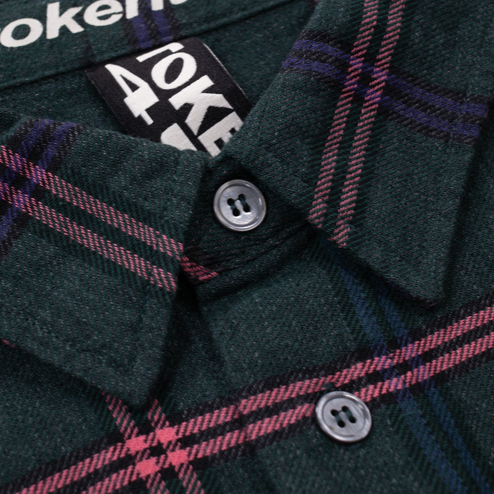 Macro studio close-up of the collar and neckline on the Token Hardware Flannel Shirt, highlighting the textured twill weave of the green, pink, and purple plaid fabric, two-hole translucent smoke grey buttons, woven black "TOKEN" neck label loop, and white printed website neckband detailing.
