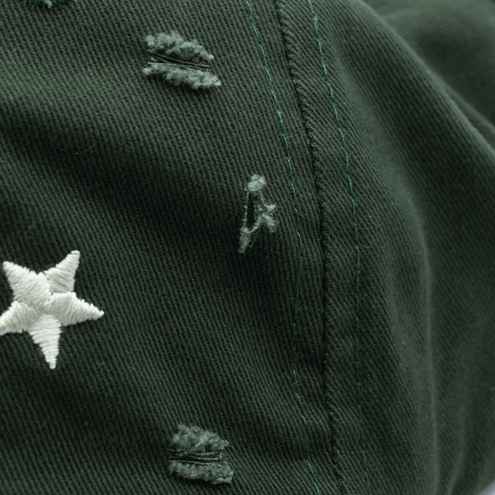 Extreme close-up macro texture shot of the midnight green cotton crown on the Token Lowkey Cap, displaying the diagonal twill weave, fine green topstitching, a crisp white embroidered star accent, and authentic distressed fabric abrasions with frayed horizontal threads.