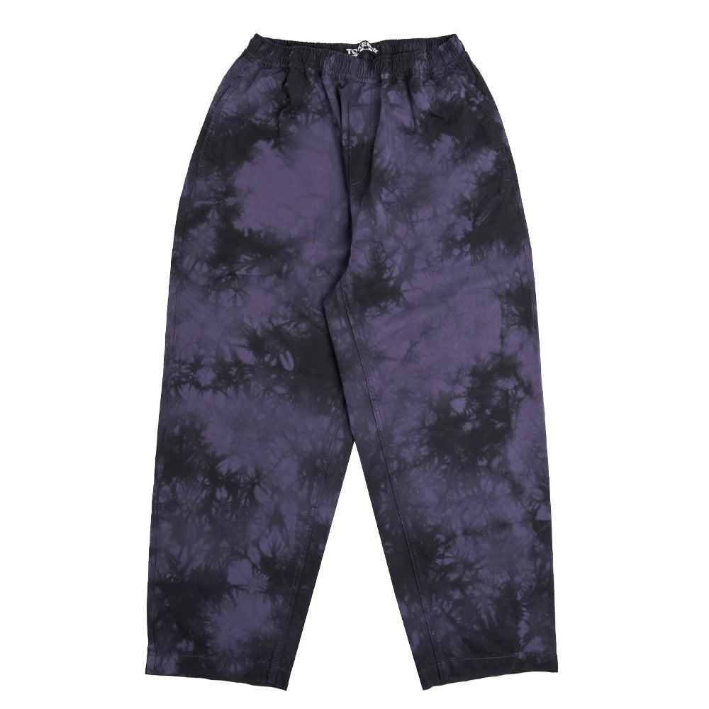 Front flat lay view of the Token Sundown Pants in purple and black tie-dye cotton twill, featuring a relaxed wide-leg skate silhouette, gathered elastic waistband, deep slanted side entry pockets, and a washed cloud-like batik pattern.