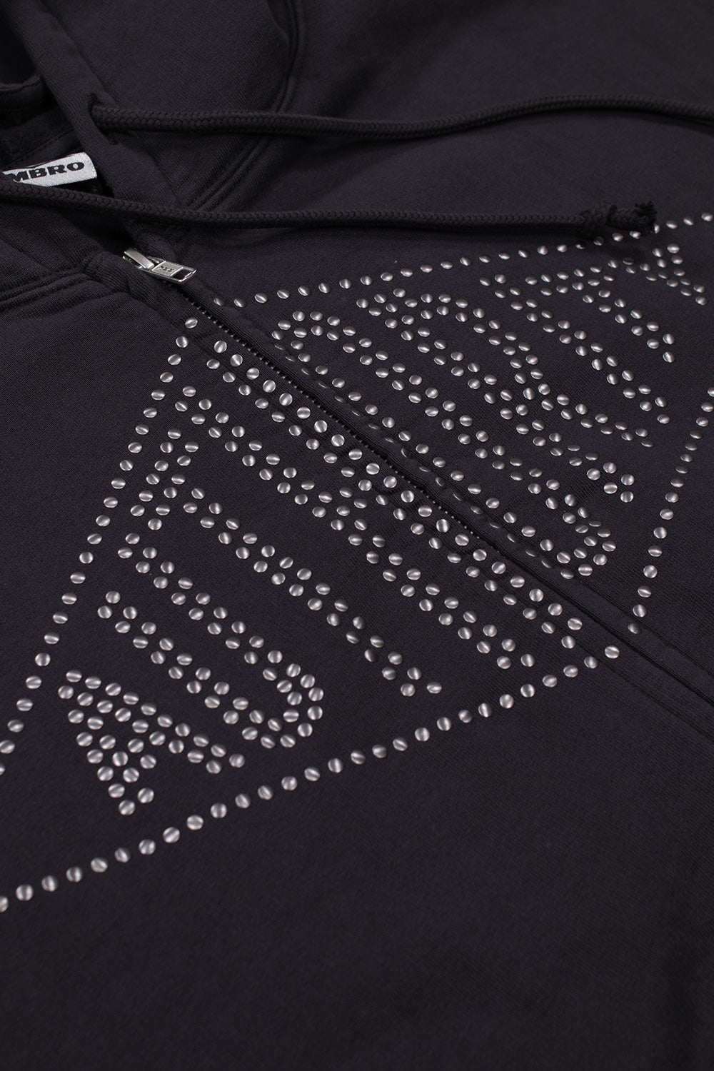 Detailed close-up shot of the chest application on the washed black Umbro Authority Zipped Hoodie, highlighting the silver round metallic domed studs arranged into a large Umbro double diamond silhouette featuring bold "AUTHORITY" block lettering alongside the central zipper track