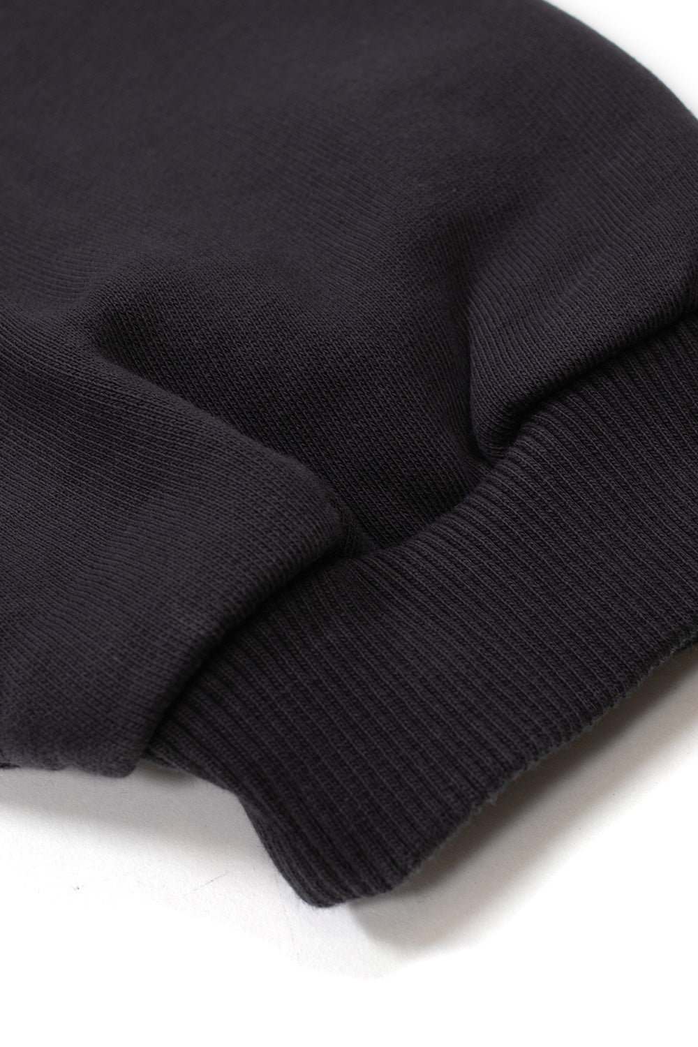 Macro detail of the wrist sleeve construction on the Umbro Authority Zipped Hoodie, showing the dense, stretchy ribbed knit cuff seamlessly attached to the gathered, washed black heavyweight cotton sweatshirt fabric