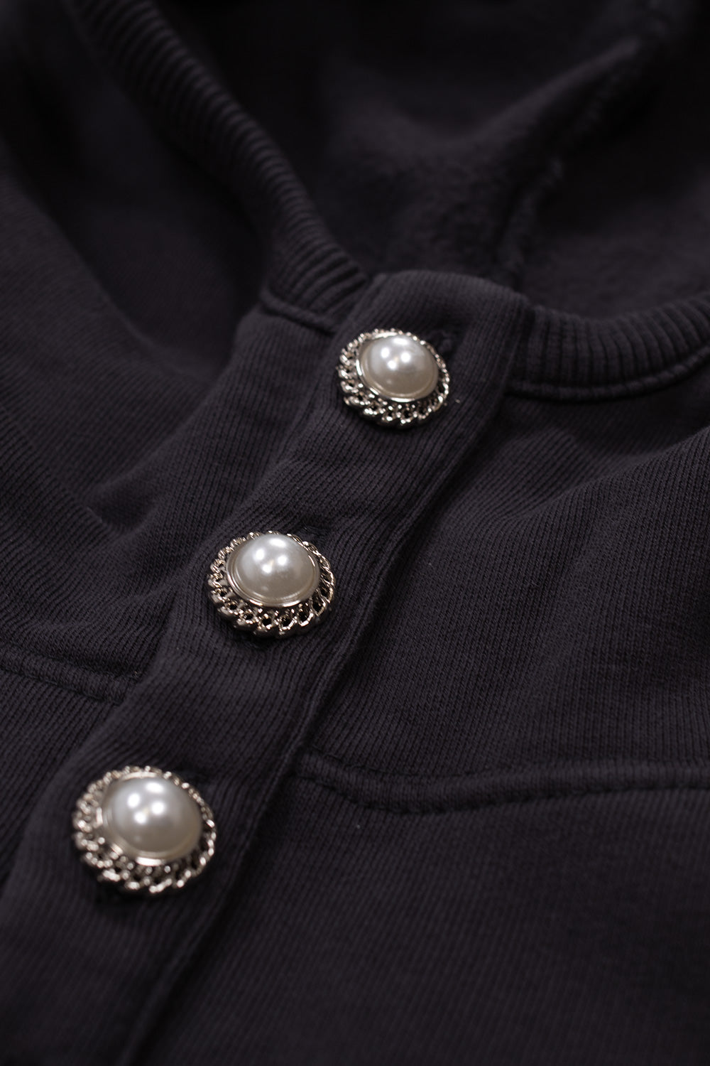 Detailed macro close-up of the front neckline placket on the Umbro Censored Pearls Hoodie, displaying ornate silver metal-rimmed domed pearl buttons sewn onto the ribbed washed black cotton collar