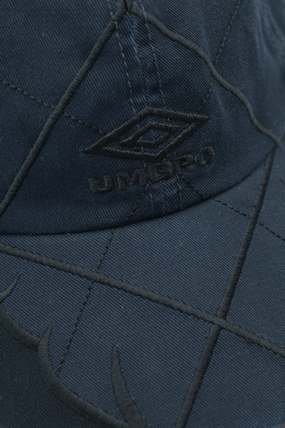 Close-up of embroidered Umbro double diamond logo on blue black anthracite Collision Cap made from durable 100 percent cotton