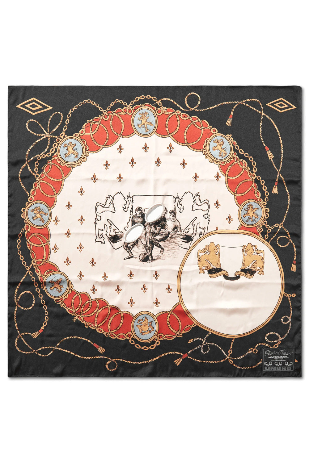 Full flat lay overview of the square Umbro Crest Masked Foulard measuring approximately 68 by 68 cm, crafted in Italy from smooth printed black and cream polyester twill, displaying an ornate equestrian and football crest graphic encircled by red braided ropes, golden tassels, chains, corner Umbro double diamonds, two oval embroidered eye holes in the center, and a black woven patch in the bottom corner