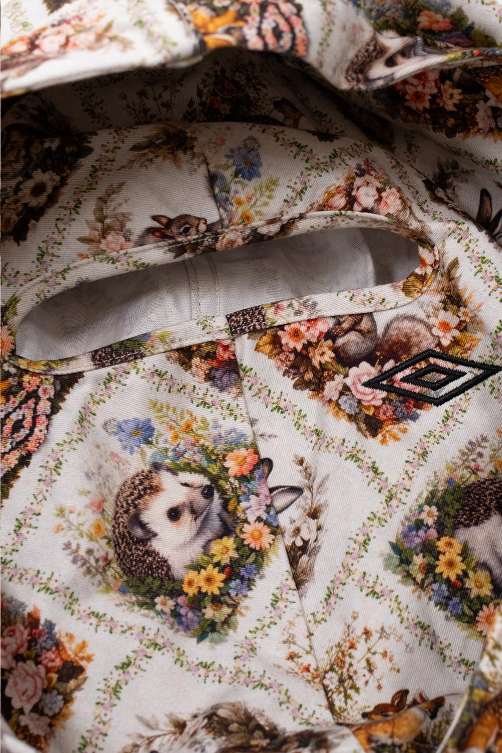 Detailed interior view of the hood on the Umbro Cub Masked Shirt, highlighting the built-in balaclava face panel with an oval finished eye-opening slit and the continuous forest animal tapestry print
