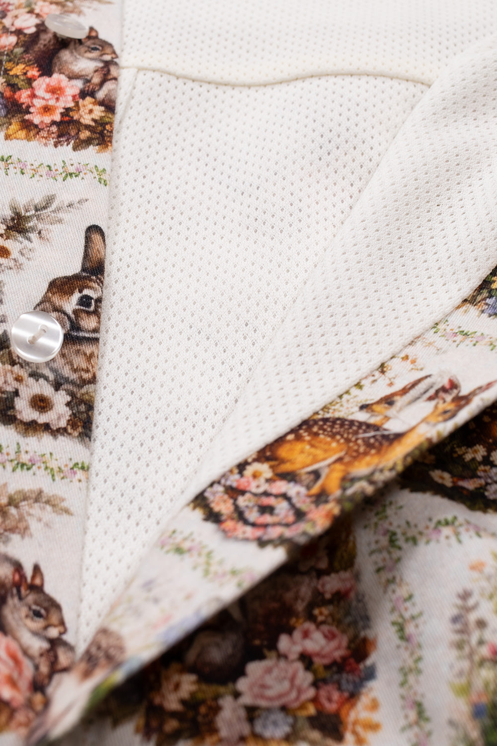 Studio close-up of the open inner lining on the Umbro Cub Masked Shirt, displaying the breathable white athletic mesh interior lining, pearlescent buttons, and the edge of the printed button placket