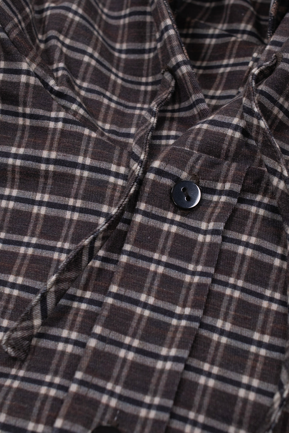Detailed close-up shot of the front button placket and collar area on the Umbro Double Plaid Jacket, showing a dark brown flat button, braided drawstrings, and the fine woven check pattern in brown, black, and cream tones