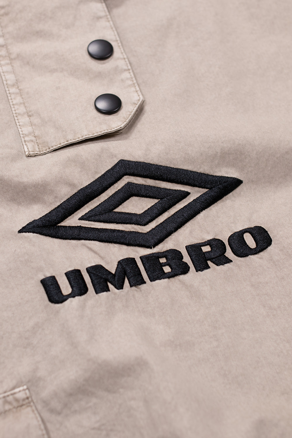 Close-up of embroidered Umbro logo on faded grey smock anorak showcasing premium streetwear craftsmanship