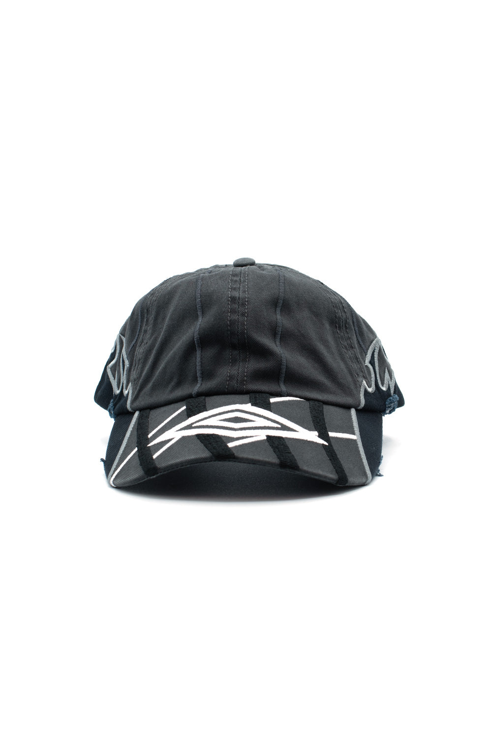 Front studio portrait of the Umbro Goalkeeper Cap in washed dark grey cotton, showcasing an unstructured 6-panel crown with vertical accent stitching, a pre-curved visor embellished with bold white and black layered tribal wave embroidery, distressed frayed details, and silver-grey embroidery wrapping around the temple panels