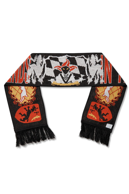 Full flat lay overview of the Umbro It All Ends In Tears Scarf measuring roughly 133 by 20 cm, made in Italy from 100% black acrylic jacquard knit, showcasing black fringe ends, red shield emblems with rampant lions, circular gold sunburst heraldic crests, and a central jester character positioned over a grey-and-white checkered flag banner with bold red blocked lettering