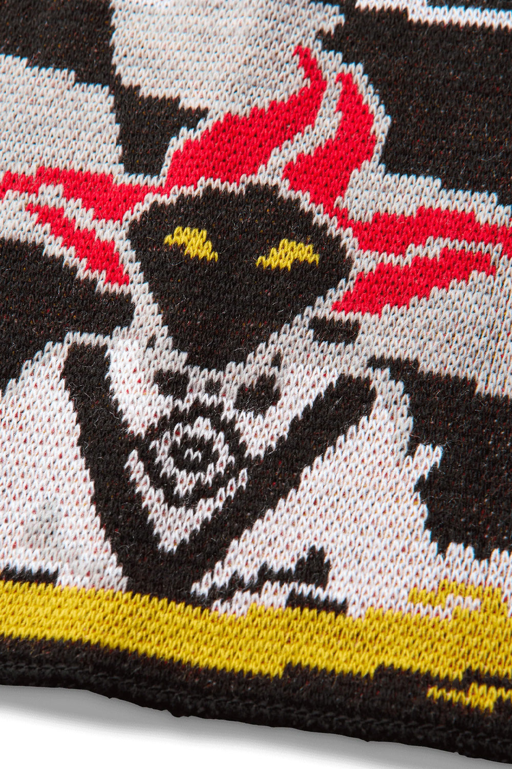 Detailed macro close-up of the jacquard knit texture on the Umbro It All Ends In Tears Scarf, displaying the tight acrylic stitch pattern forming the hooded jester face with piercing yellow eyes, red cap tassels, white textured collar, and yellow banner border