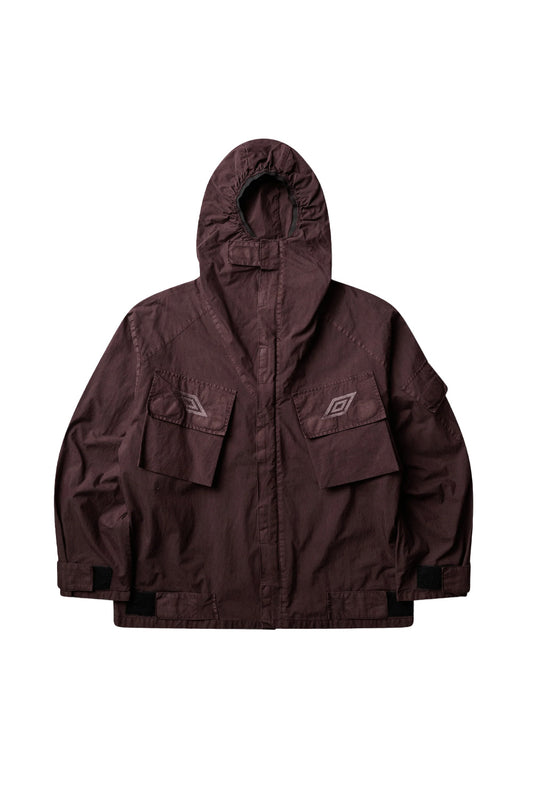 Front flat lay view of the Umbro Midfield Jacket in washed plum grey, showcasing a technical utility silhouette, high-neck storm hood with hook-and-loop chin closure, storm flap concealing the front zipper, angular bellowed cargo chest pockets with tonal embroidered double diamonds, arm pocket, and adjustable hem straps