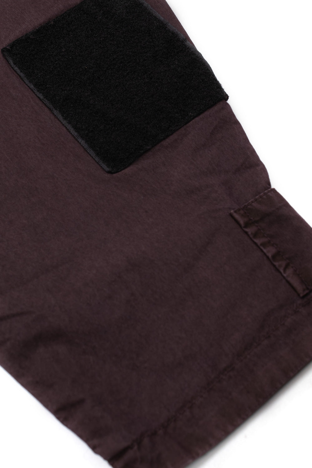 Macro detail of the lower sleeve on the Umbro Midfield Jacket, showcasing a black rectangular velcro hook-and-loop patch above an adjustable fabric cuff cinch tab set against the washed plum purple textile