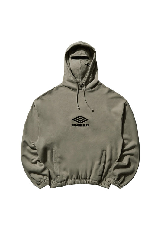 Front flat lay view of the Umbro OG Logo Mask Hoodie in dark greige taupe, showcasing a boxy oversized heavyweight fleece silhouette with elasticated gathered hem and cuffs, vertical side welt pockets, drawstring hood, an integrated matching fabric balaclava mask with a horizontal eye slit, and a black satin-embroidered classic Umbro double diamond wordmark logo across the center chest