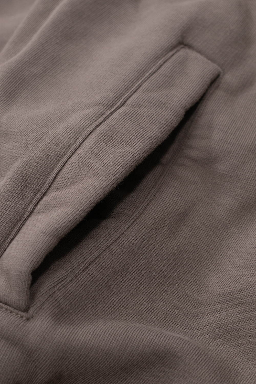 Studio close-up view of the vertical side entry welt pocket on the dark greige Umbro OG Logo Mask Hoodie, displaying the clean bar-tacked edge stitching and the dense diagonal twill-like loopback fleece texture