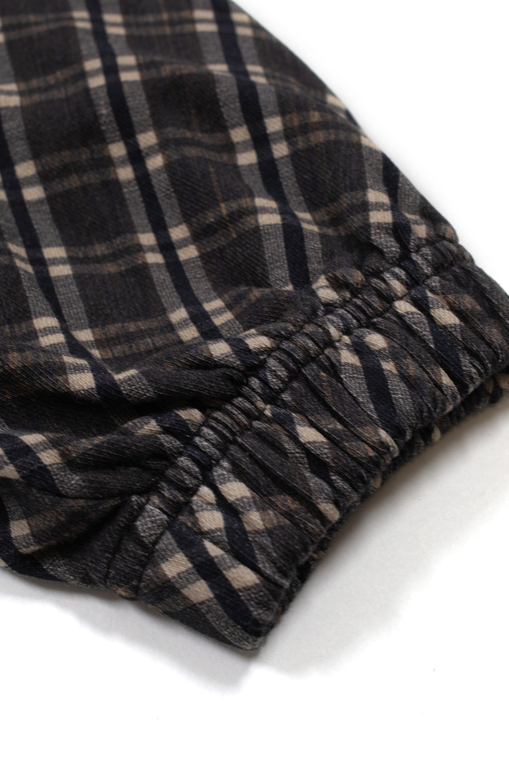 Macro studio close-up of the gathered elasticated sleeve cuff on the brown Umbro Plaid Masked Hoodie, highlighting the fine diagonal twill texture of the tartan check pattern and the pleated gathered edge stitching