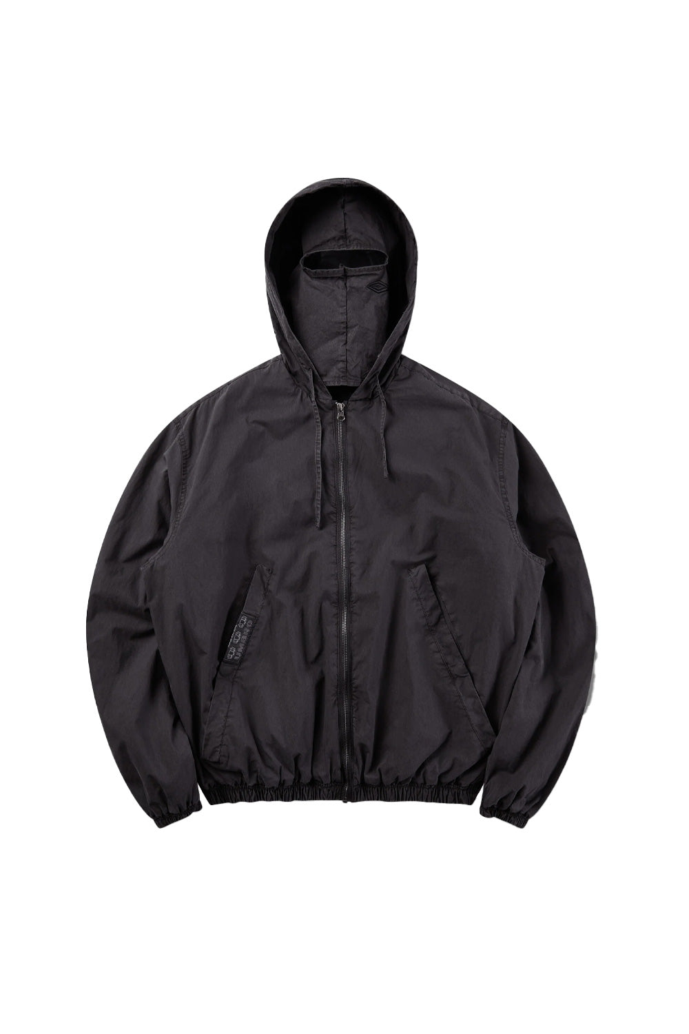 Front flat lay view of the Umbro Sunday Masked Jacket in washed black, featuring a lightweight cotton blouson silhouette with full front zip closure, elasticated gathered hem and cuffs, angled welt side pockets, a branded woven tape label on the right pocket, and a hood equipped with an integrated matching fabric face mask with an eye opening slit