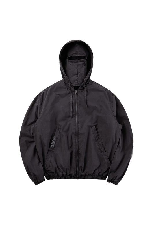 Front flat lay view of the Umbro Sunday Masked Jacket in washed black, featuring a lightweight cotton blouson silhouette with full front zip closure, elasticated gathered hem and cuffs, angled welt side pockets, a branded woven tape label on the right pocket, and a hood equipped with an integrated matching fabric face mask with an eye opening slit