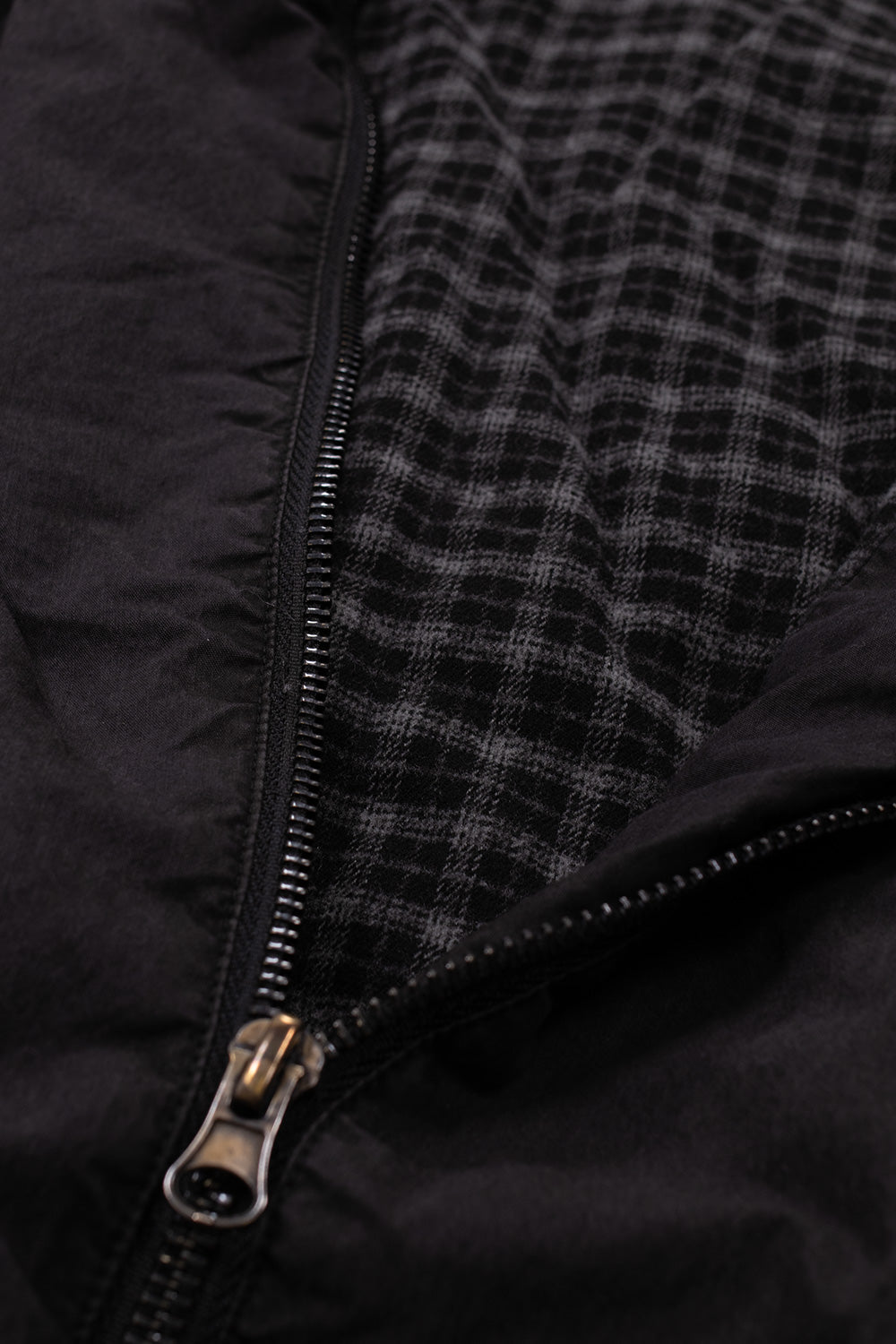 Detailed view of the unzipped front placket on the Umbro Sunday Masked Jacket, displaying the antique silver metal zipper slider, robust teeth, and the dark grey-and-black yarn-dyed tartan check flannel lining