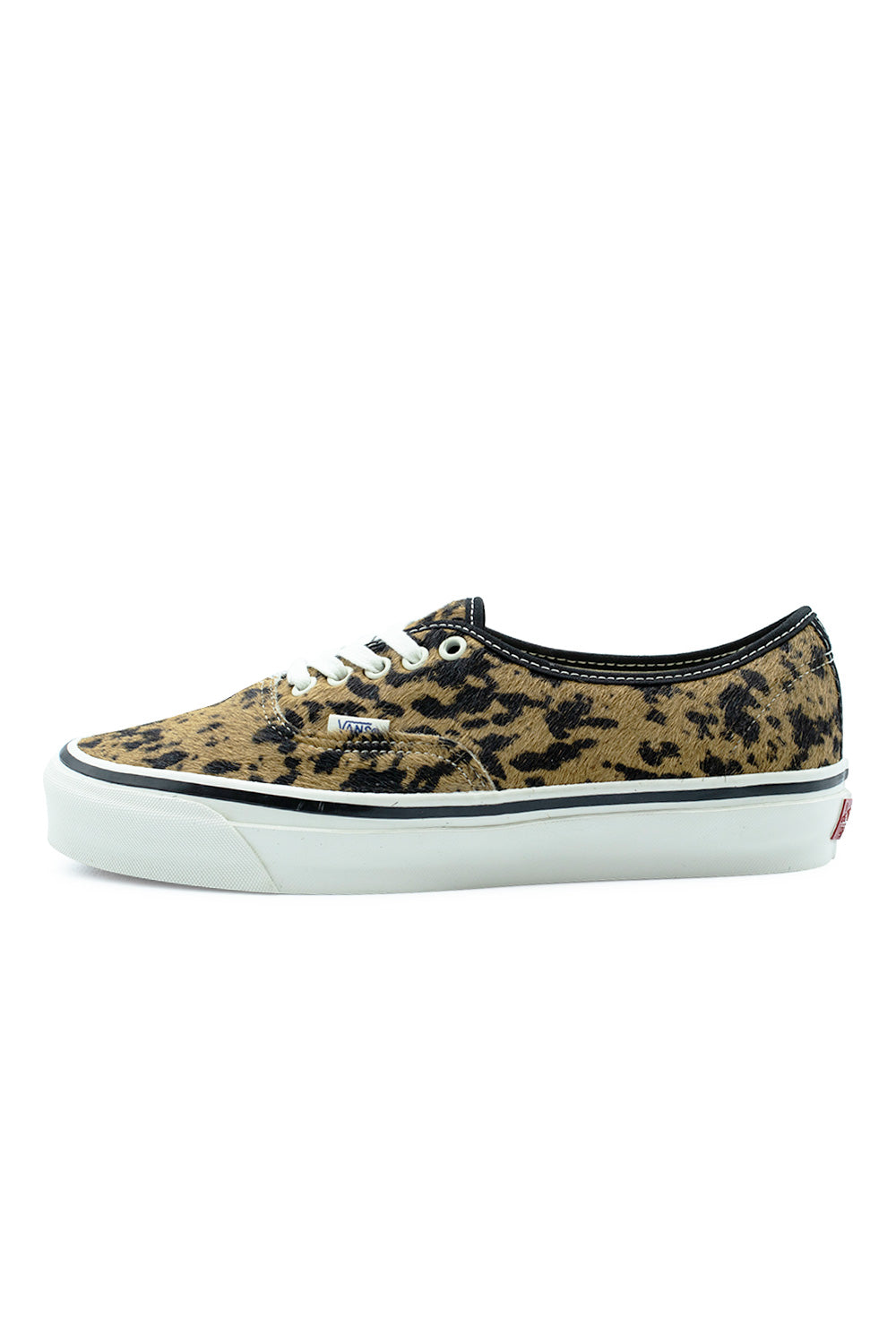 Lateral side profile view of the Vans LX Authentic 44 sneaker in Cow / Marshmallow, featuring a textured brown and black cow-print pony hair upper, black collar piping, white cotton laces through white metal eyelets, small blue woven Vans flag label, and a glossy marshmallow vulcanized midsole with a black foxing stripe.