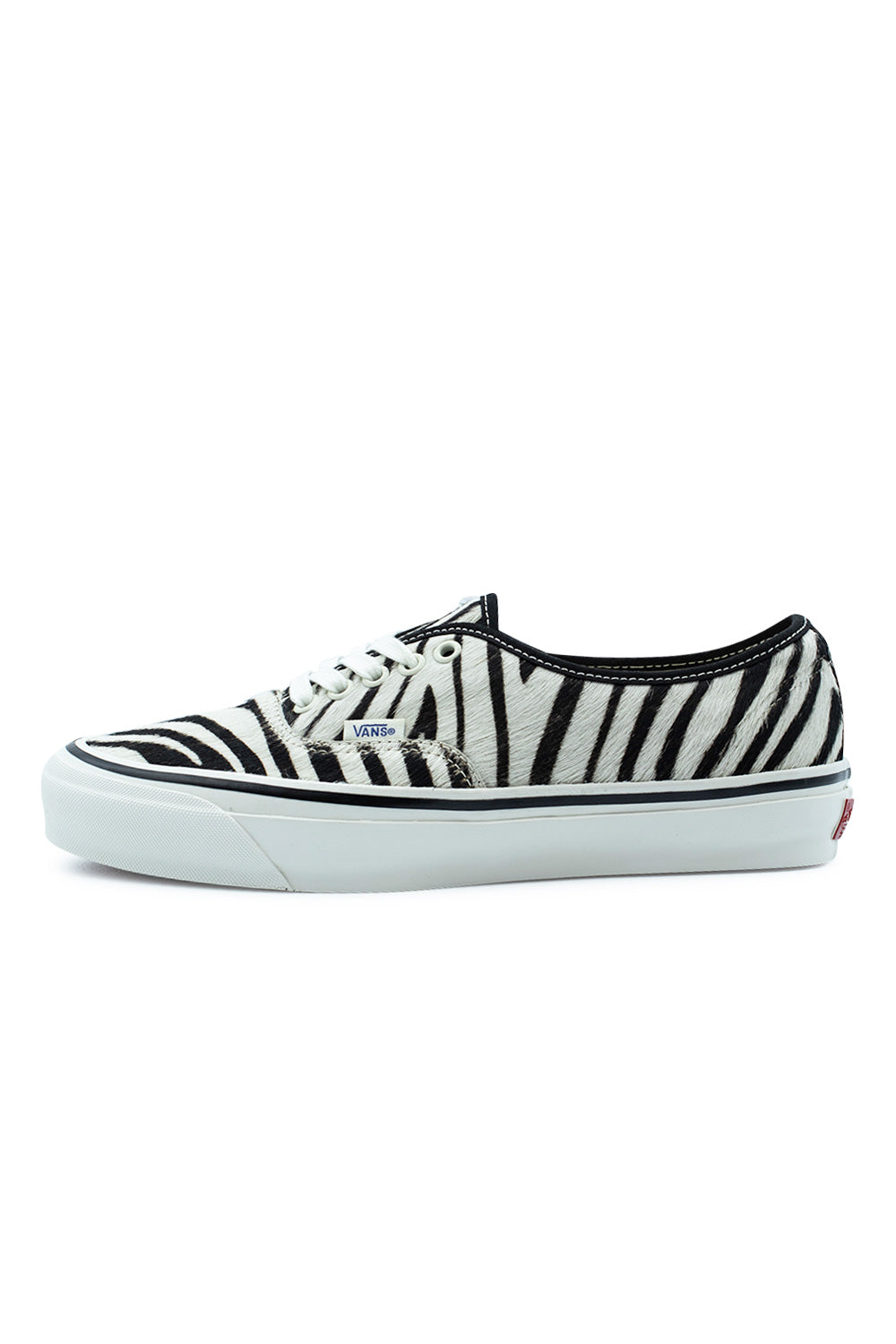 Lateral side profile view of the Vans LX Authentic 44 sneaker in Zebra / Marshmallow, showcasing the monochrome black-and-white striped pony hair cowhide upper, black collar trim, clean white cotton laces through white metal eyelets, small blue woven Vans flag label, and a glossy marshmallow vulcanized midsole with a black foxing line.