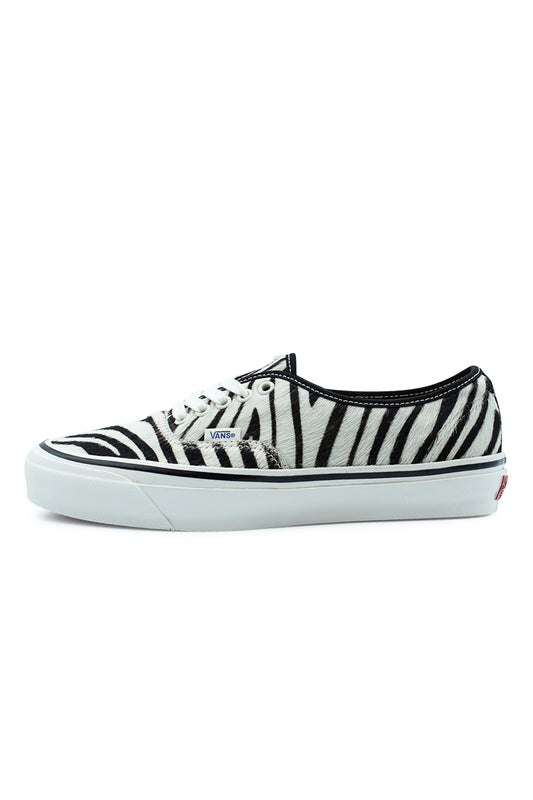 Lateral side profile view of the Vans LX Authentic 44 sneaker in Zebra / Marshmallow, showcasing the monochrome black-and-white striped pony hair cowhide upper, black collar trim, clean white cotton laces through white metal eyelets, small blue woven Vans flag label, and a glossy marshmallow vulcanized midsole with a black foxing line.