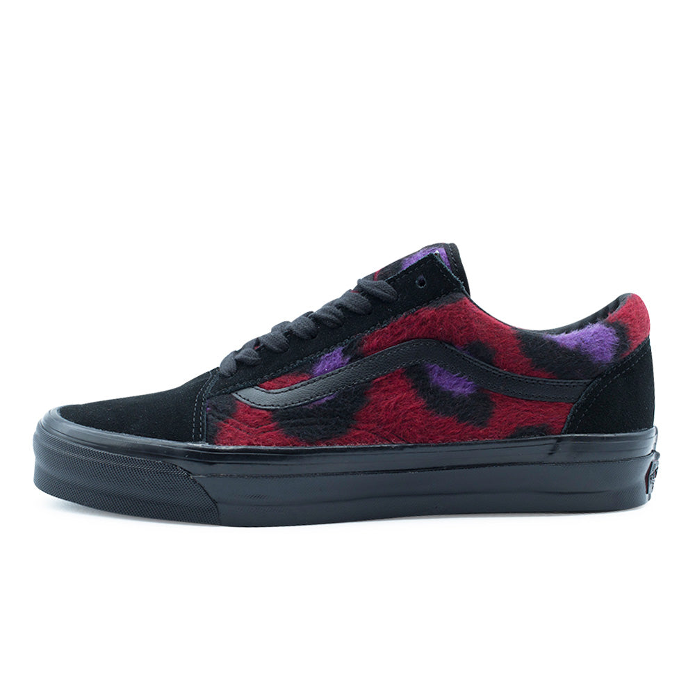 Lateral profile studio view of the Vans LX Old Skool shoe in Leopard Black / Multi, showcasing the low-top skate silhouette with tactile faux-fur fleece quarter panels in vibrant red, purple, and black leopard print, black suede toe box and heel counter, black pebbled leather Jazz Stripe, and high-gloss black vulcanized rubber foxing.