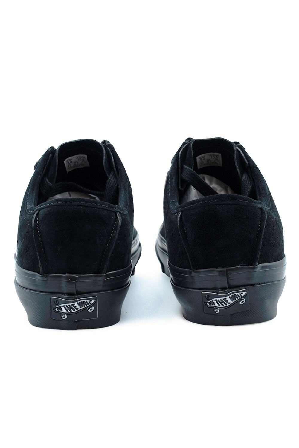 Rear view of the heels of the Vans LX SF Moc Low sneakers in Black / Black, highlighting the solid black suede heel counters with tonal arc stitching, low-cut padded ankle collars, and black-on-white vintage Vans Off The Wall skateboard heel license plates.