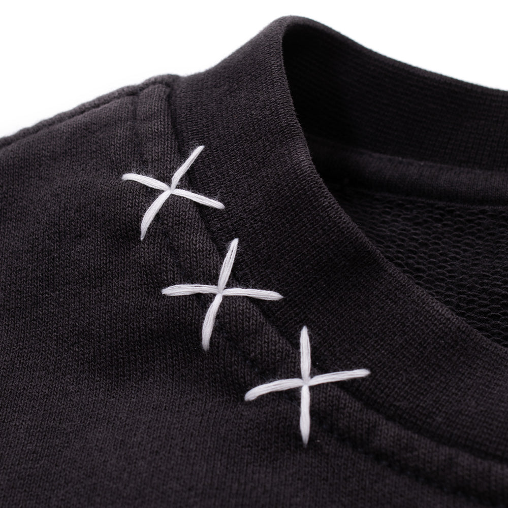 Detailed macro perspective of the right neckline on the Vans OTW x Chito Sweatshirt, capturing the heavy, contrast white thread hand-sewn into three large 'XXX' cross-stitch motifs bridging the ribbed collar and shoulder seam.