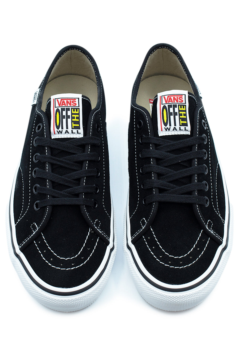 Top-down perspective of a pair of Vans Skate AVE Classic pro sneakers, showcasing the black suede toe box with curved white double stitching, black laces, and woven Vans Off The Wall tongue labels with yellow and red vintage branding.