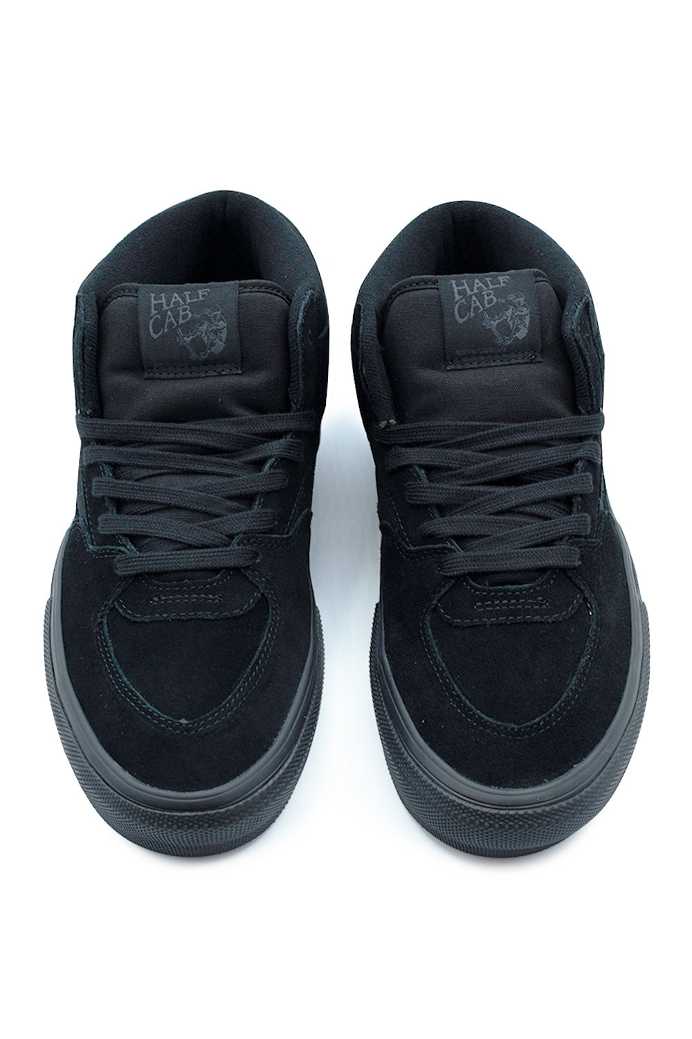 Top-down view of a pair of all-black Vans Skate Half Cab shoes, displaying the durable black suede toe caps with tonal reinforcement stitching, breathable canvas panels, flat black laces, and padded mesh tongues with tonal woven Steve Caballero Half Cab logo patches.