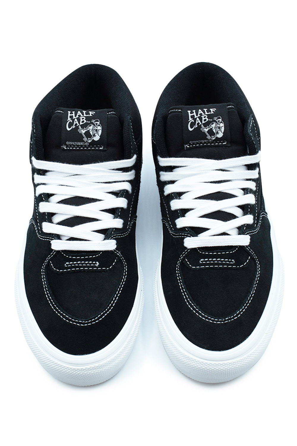 Top-down view of a pair of black and white Vans Skate Half Cab shoes, displaying the reinforced suede toe caps accented by double white stitch lines, flat white cotton laces, and padded black mesh tongues with heritage woven Steve Caballero Half Cab logo patches.