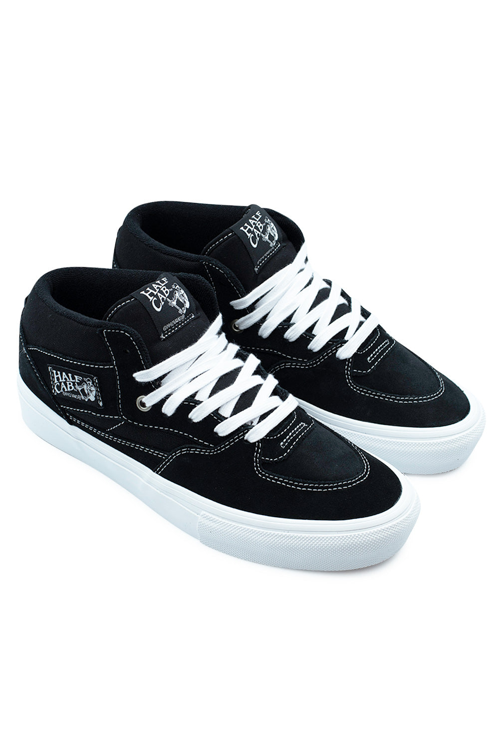 Elevated three-quarter perspective studio shot of the Vans Skate Half Cab shoes in Black / White, highlighting the iconic 1992 skate mid-top silhouette, durable suede and canvas construction, white contrast elements, and high-rebound PopCush footbeds.