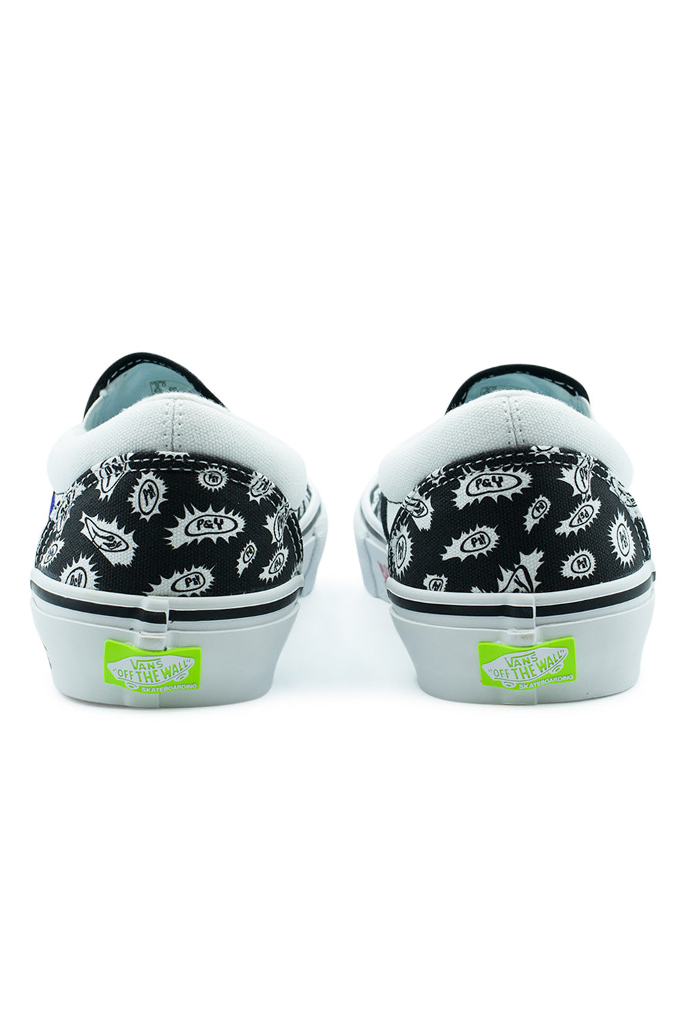Rear perspective shot of the heels of the Vans X Punk And Yo Skate Slip-On sneakers, displaying the printed black-and-white canvas heel counters, clean double-stitched center heel seams, thick white rubber foxing, and the bright neon green rubber Vans Off The Wall Skateboarding license plate heel tabs