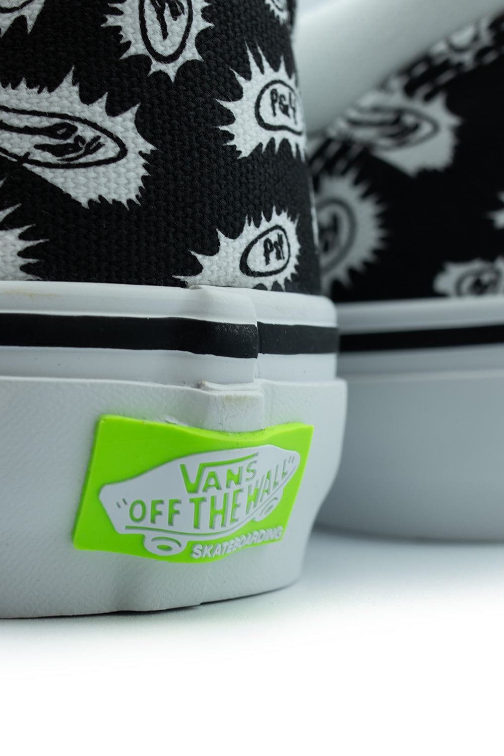 Close-up shot of the heel bumper on the Vans X Punk And Yo Skate Slip-On, highlighting the textured white rubber foxing tape and the contrasting neon lime green molded "VANS OFF THE WALL SKATEBOARDING" license plate heel scab