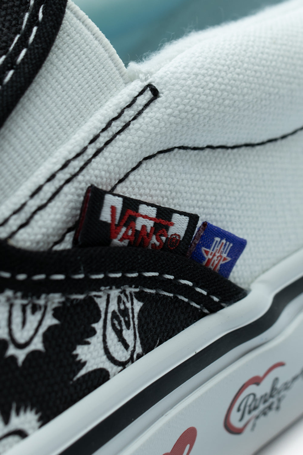 Macro detail of the lateral collar seam on the Vans X Punk And Yo Skate Slip-On, featuring the dual-sided woven flag label showing the classic black-and-white Vans checkerboard flag paired with a purple Punk and Yo logo tag
