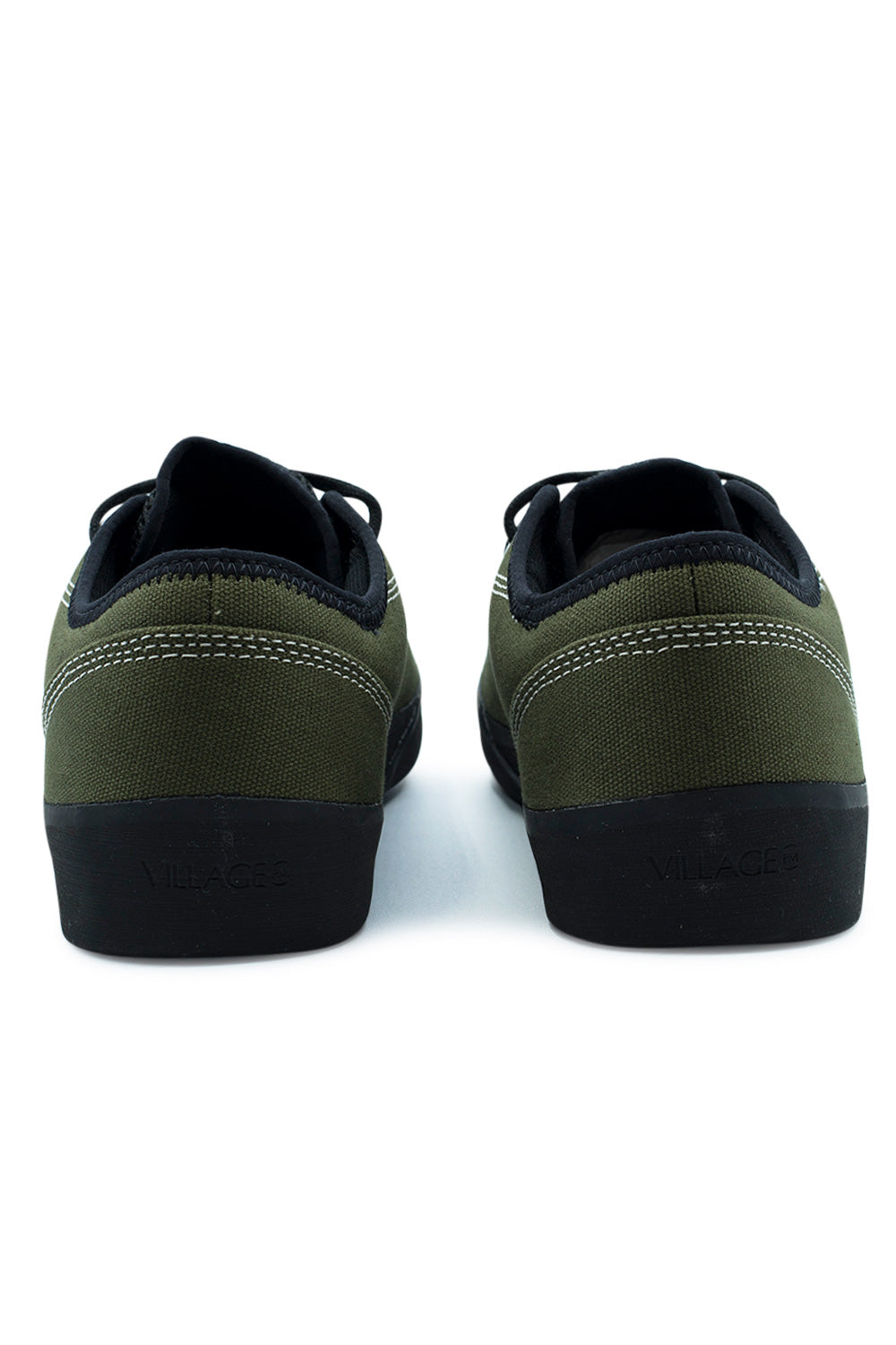 Rear studio view of the heels of the Village PM 1.30PM sneakers, showing the textured olive canvas heel construction with curved white contrast stitching, padded black collar trim, clean heel silhouette without pull tabs, and thick black rubber heel foxing embossed with subtle "VILLAGE" branding.