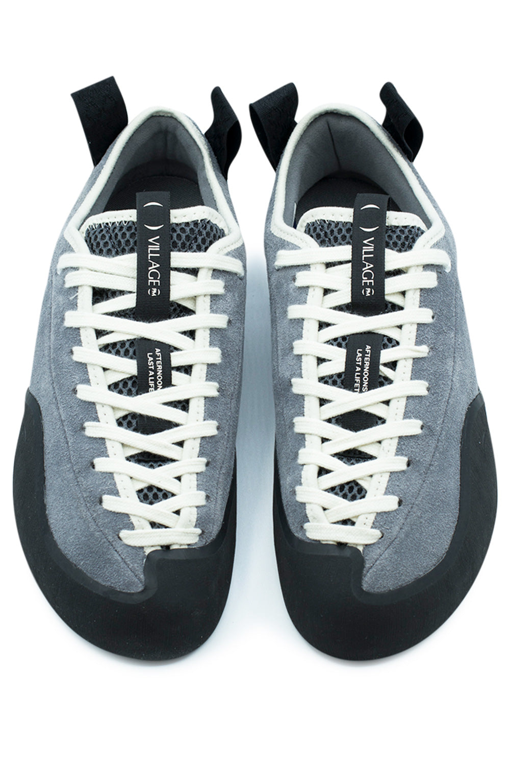 Top-down view of a pair of Village PM 1PM skate shoes, showing the anatomical asymmetrical toe shape, protective wrapped black climbing rubber toe cap, extended toe-to-collar off-white lacing through punched eyelets, dark grey open-mesh tongues, and black woven "VILLAGE PM" tongue pull tags[cite: 90].