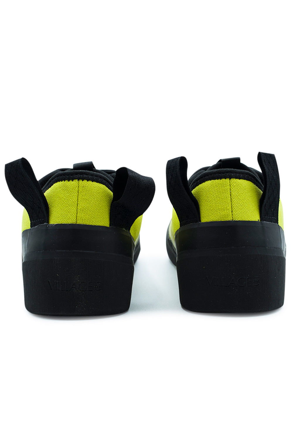 Rear perspective view of the heels on the Village PM 1PM Lime LTR sneakers, showcasing the neon lime canvas heel counter construction, black padded collar edge binding, dual heavy-duty black webbing pull loops, and high black rubber heel wrap embossed with tonal "VILLAGE" block lettering.