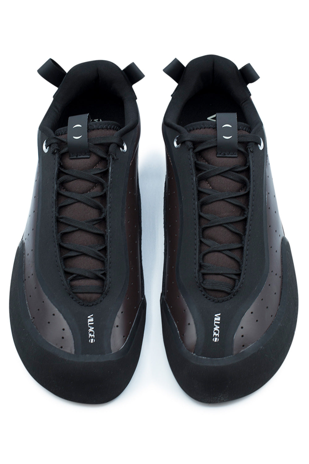 Top-down studio shot of a pair of Village PM 2PM skate shoes, showing the anatomical asymmetrical shape with angular toe box, protective matte black climbing rubber toe caps, extended black lace system partially concealed beneath protective rubber rand borders, perforated maroon side panels, and branded tongue pull tabs printed with white "VILLAGE" script.