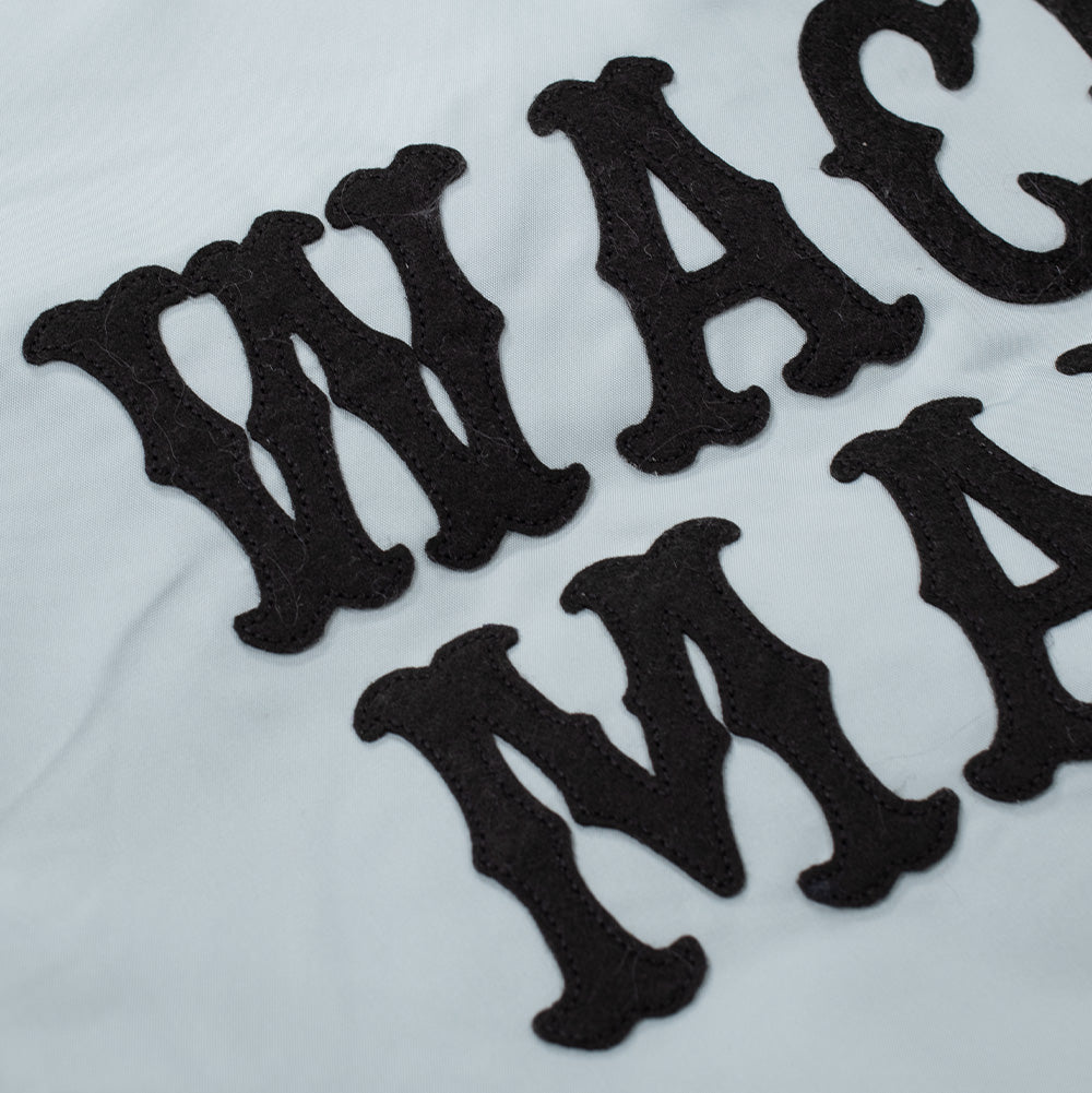 Extreme macro close-up of the back graphics on the grey Wacko Maria Coach Jacket, showing the textured black wool felt material and tonal satin-stitch edge detailing on the western gothic "WACKO MARIA" letter patches.